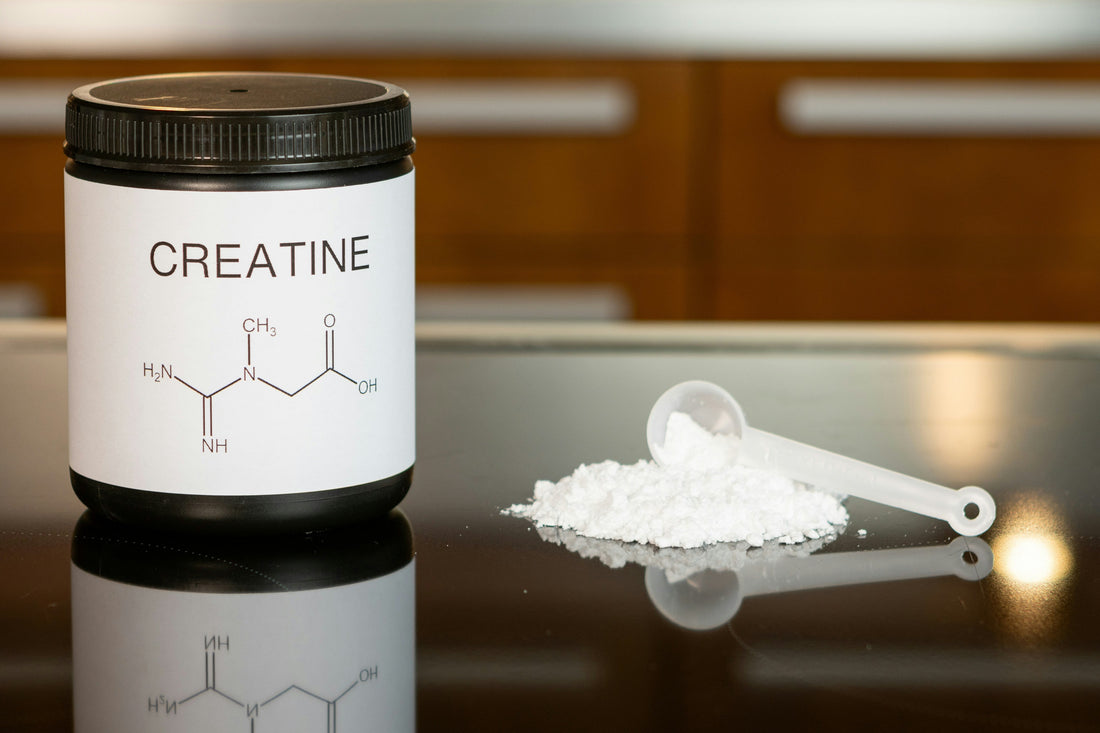 Creatine supplement jar with chemical formula, white powder, and scoop on a reflective surface.