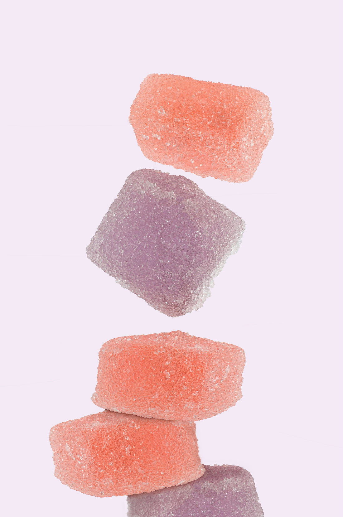 Stack of vibrant, sugar-coated peach and lavender gummy supplements.